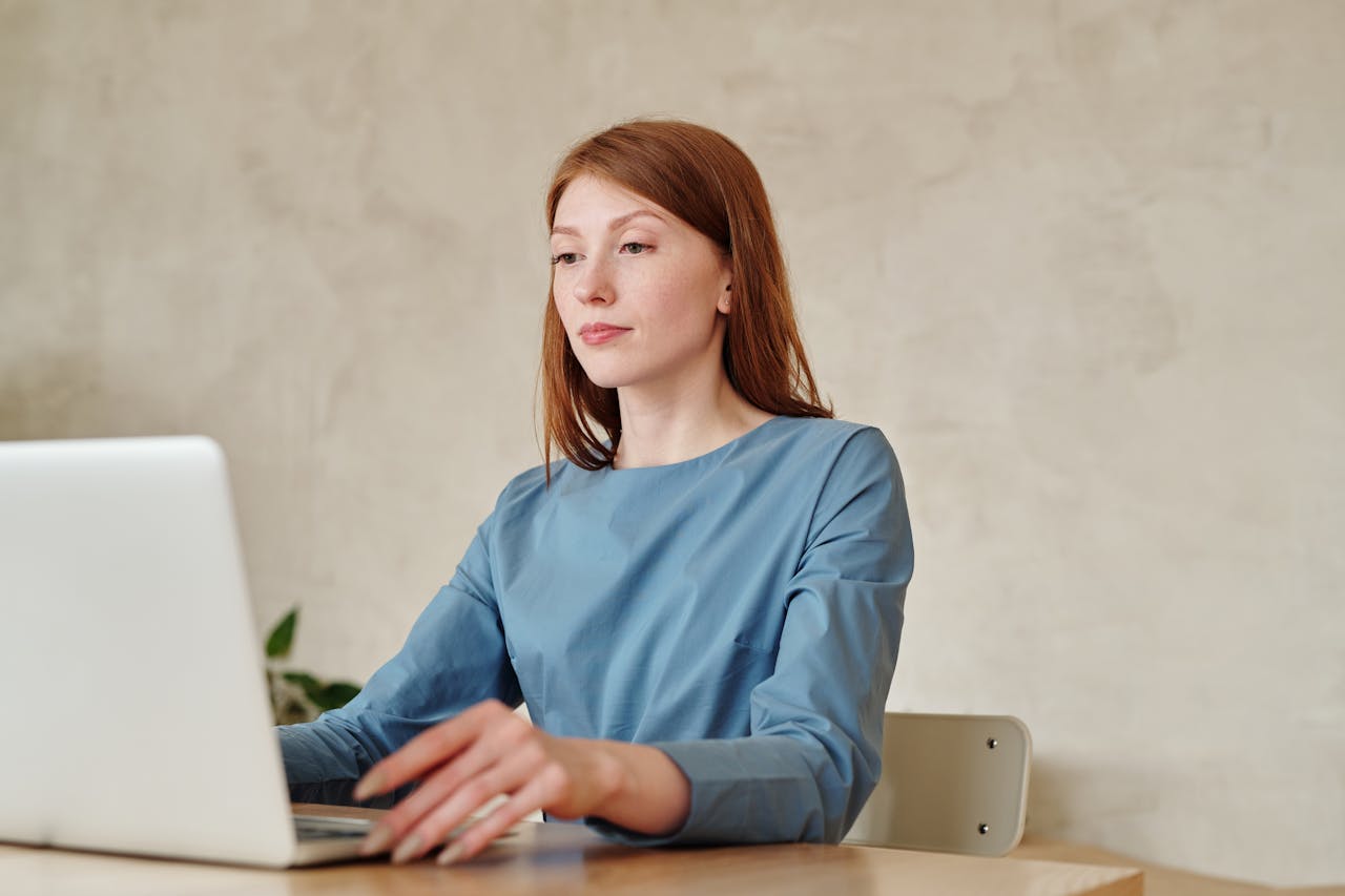 Caucasian woman in blue shirt working on a laptop indoors at home.